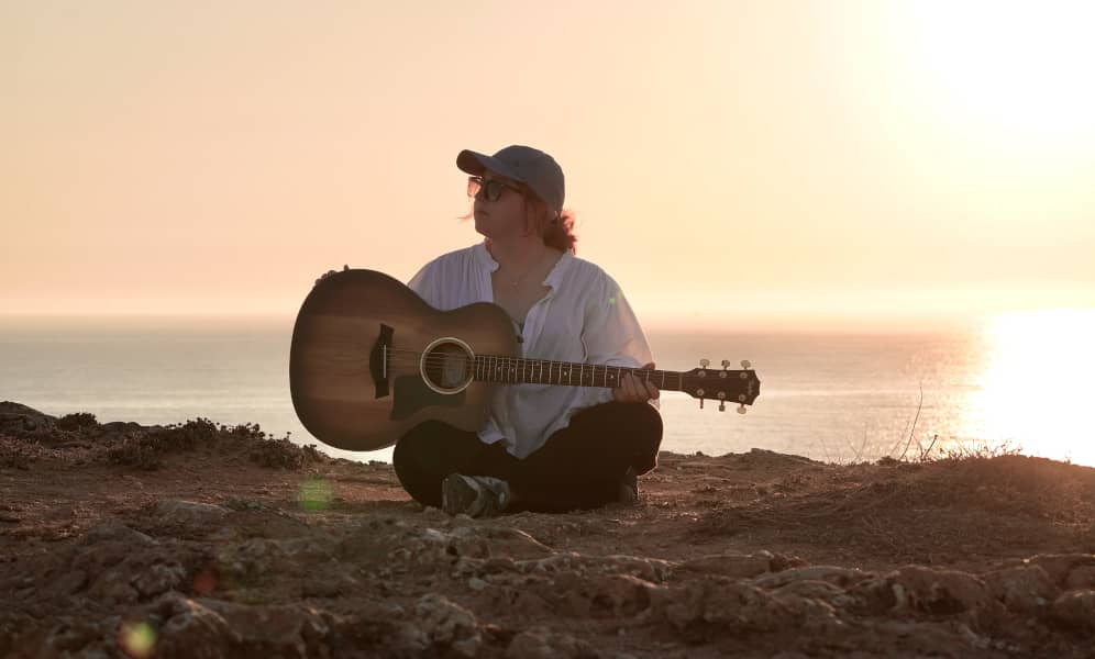 Die Singer-Songwriterin Anna Jakob sitzt mit ihrer Gitarre bei Sonnenuntergang am Meer