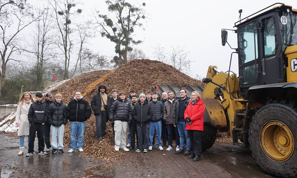 Eine Gruppe von Schülern vor den Holzhackschnitzeln des Biomasseheizkraftwerks