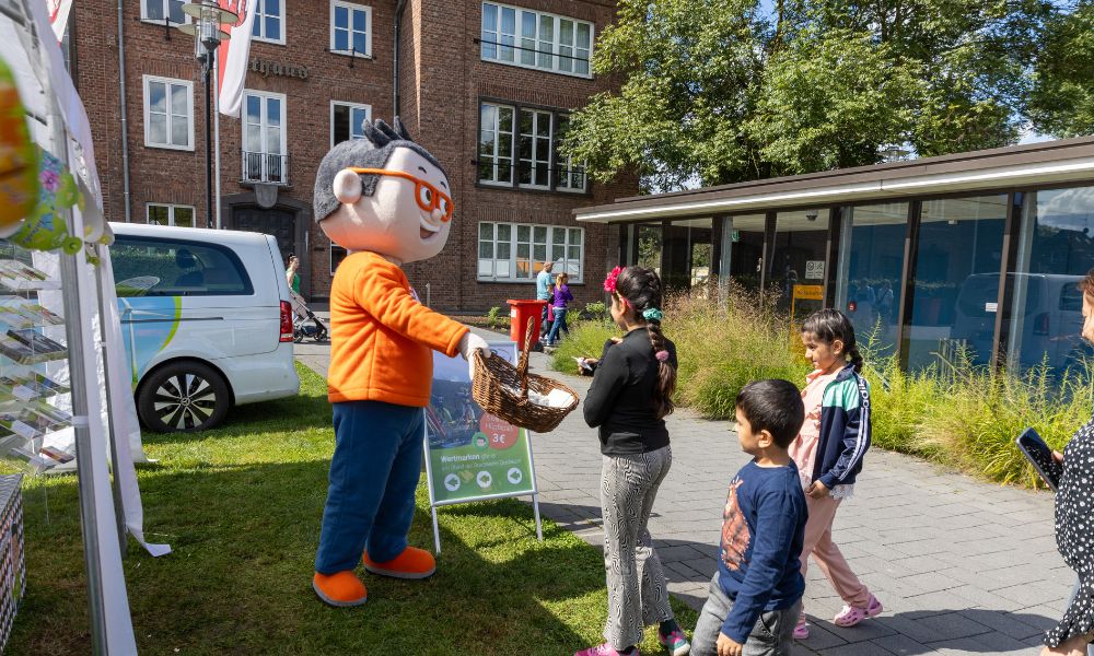 Das DIN-Maskottchen verteilt Gummibärchen an Kinder