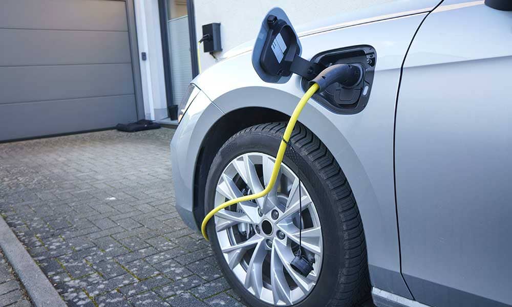 Ein Auto lädt mit Stecker an der Seite vor einem Garagentor