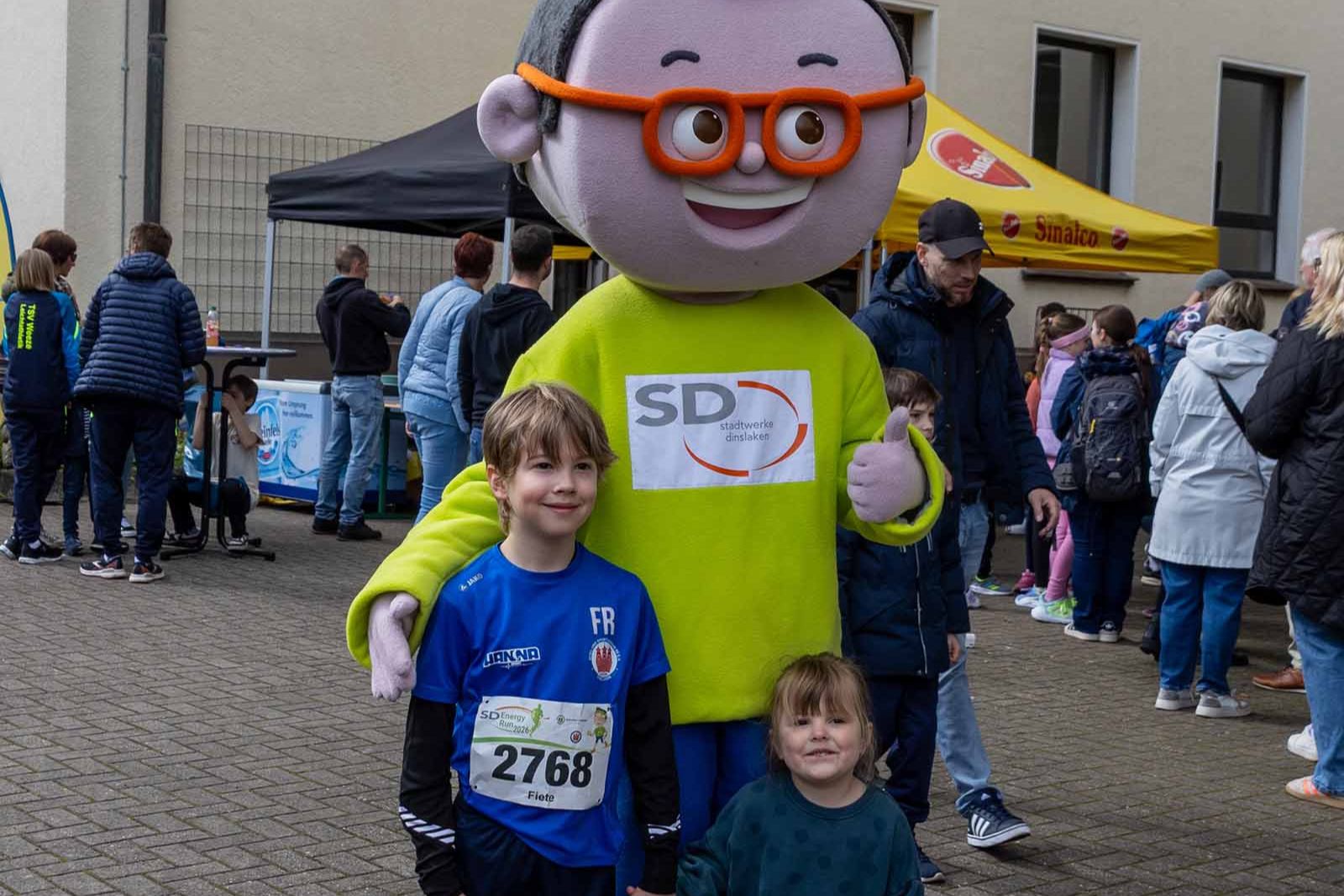 DIN-Maskottchen posiert mit zwei Kindern