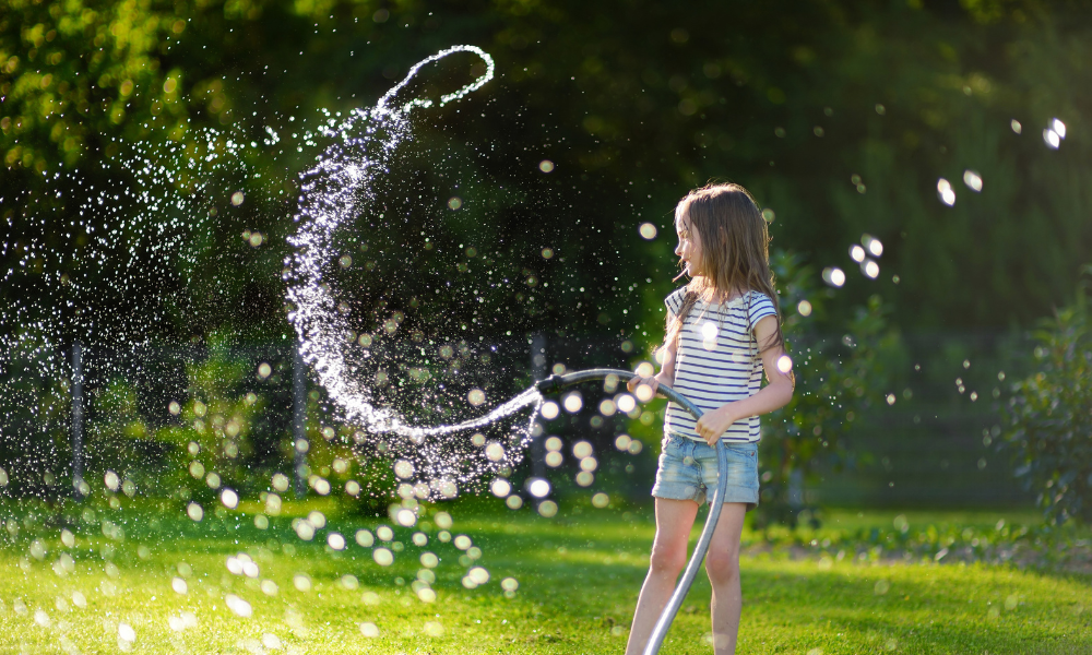 Mädchen verspritzt mit Wasserschlauch Wasser im Garten