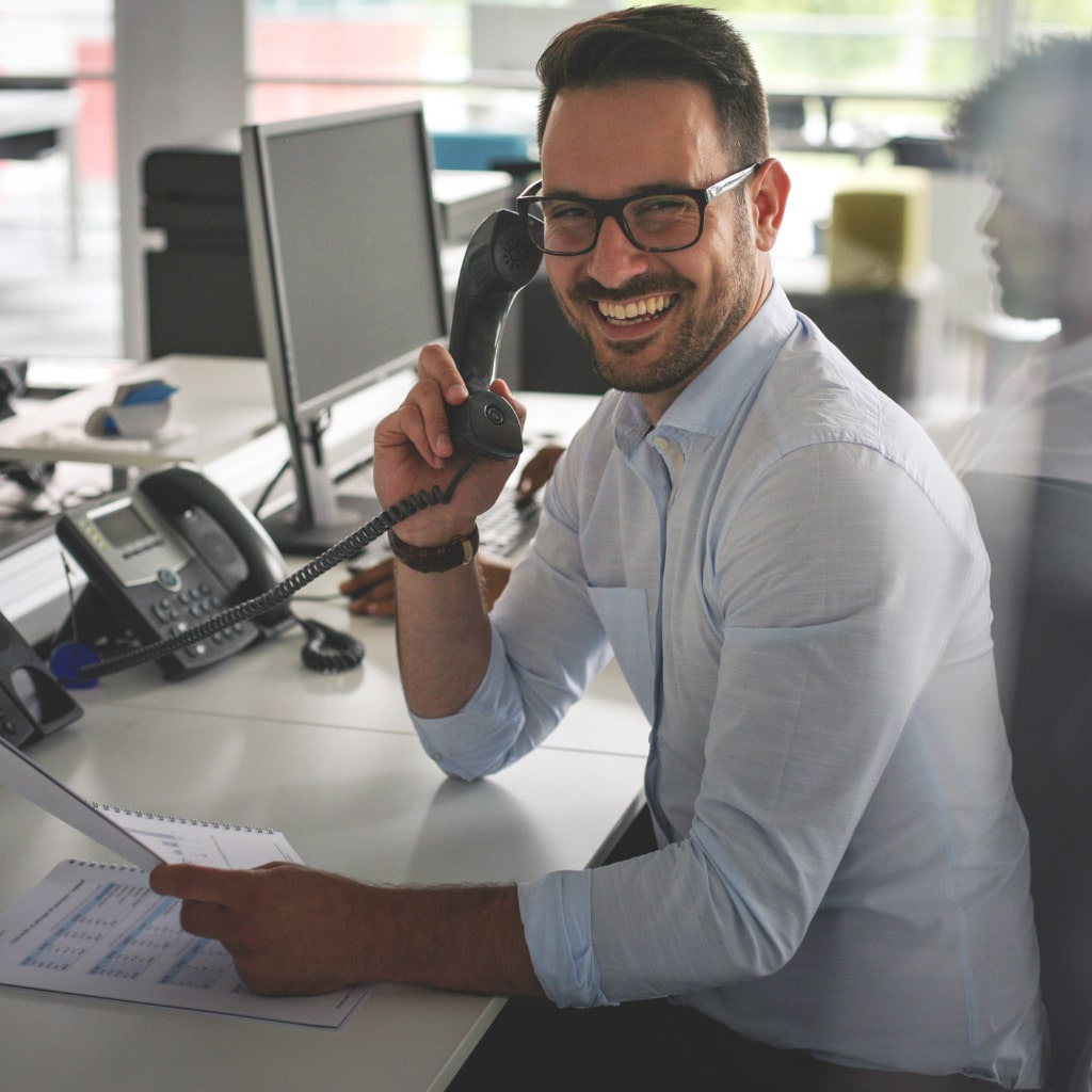 Mann mit Telefonhörer am Ohr lacht und hat Unterlagen in der Hand.