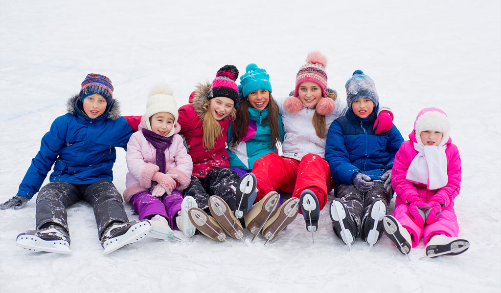 Reihe sitzender Kinder auf Eisfläche mit Wintersachen und Schlittschuhen an