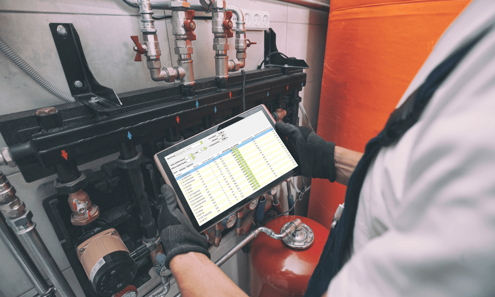 Mann hält Tablet in der Hand mit Schutzhandschuhen und hält es vor ein Heizungssystem.