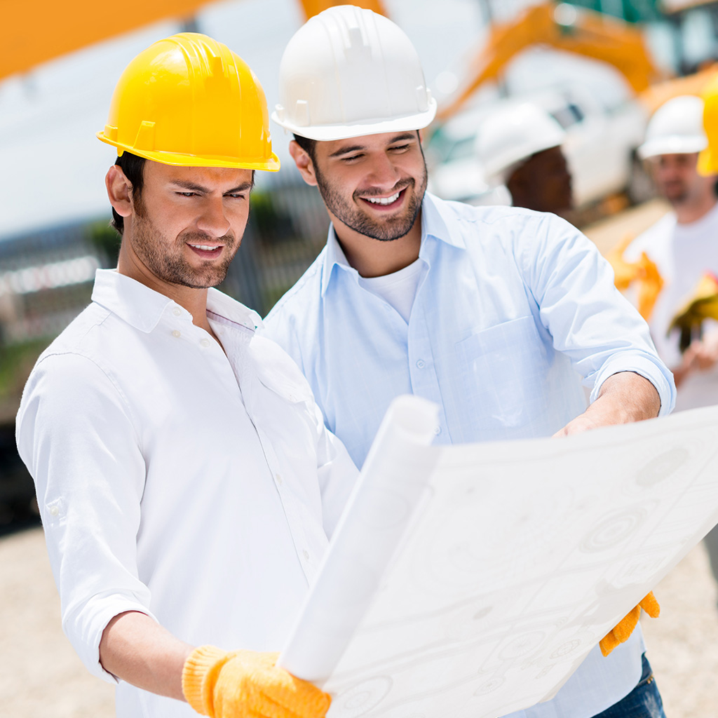 Zwei Bauingenieure mit Schutzhelmen begutachten einen Bauplan auf einer Baustelle, im Hintergrund arbeiten weitere Bauarbeiter mit Baggern und Maschinen