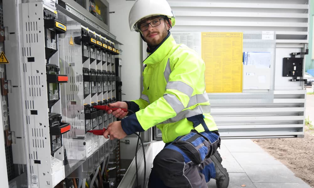 Ein Mitarbeiter aus der Technik kniet vor einer Trafostation