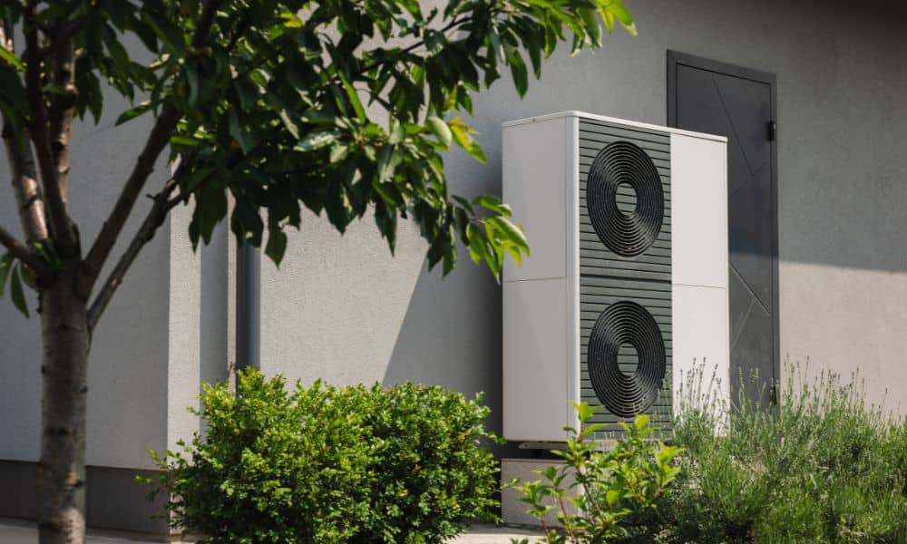 Wärmepumpe vor einem Haus mit Sträuchern und Baum