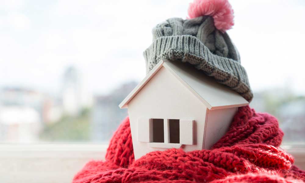 Modellhaus aus Holz ist mitSchal und Mütze warm eingepackt